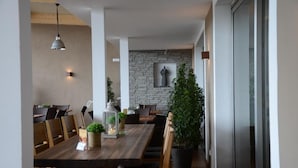 A dining area with a wooden table, chairs, pendant lighting, a stone wall, and a potted plant. - Hotel Rheinstein (Ruedesheim am Rhein)