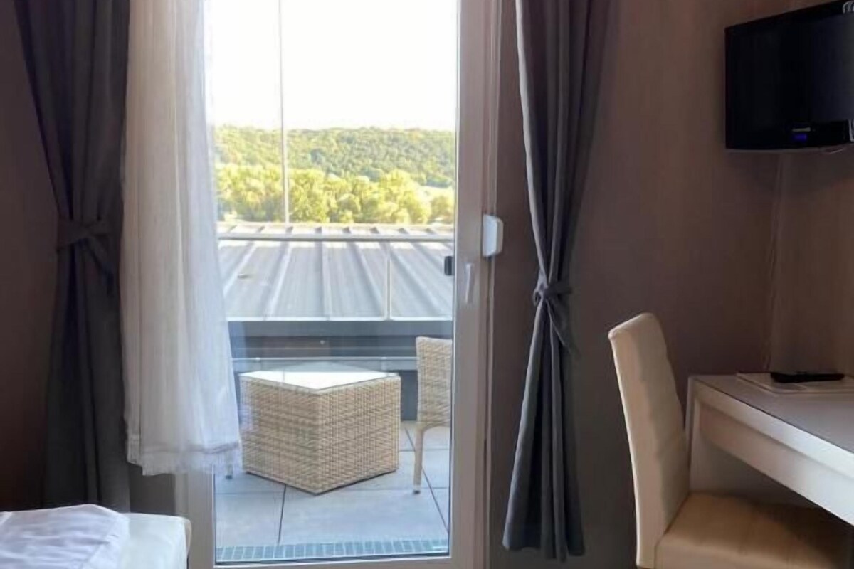 A hotel room with a bed, a desk, a chair, a television, and a sliding glass door leading to an outdoor area with a wicker chair and a table.