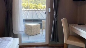 A hotel room with a bed, a desk, a chair, a television, and a sliding glass door leading to an outdoor area. - Hotel Rheinstein (Ruedesheim am Rhein)