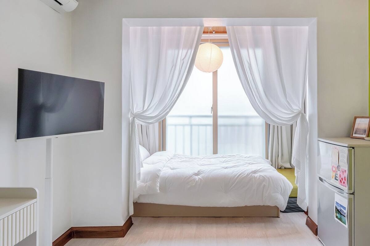 Un dormitorio con cama, cortinas, televisor, armario y ventana.