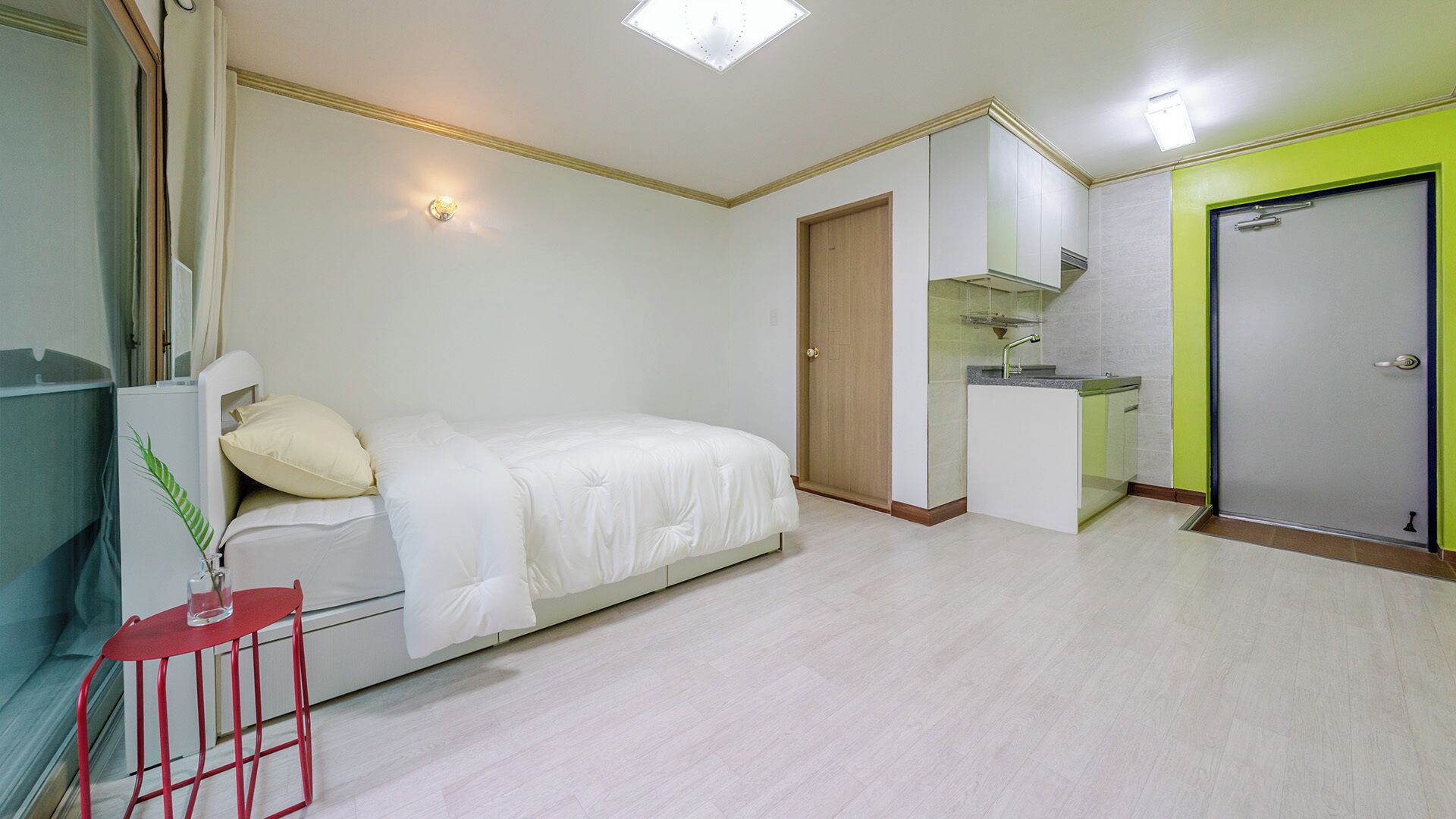 A bedroom with a bed, a small desk, a mirror, a wardrobe, and a bathroom with a sink and mirror.
