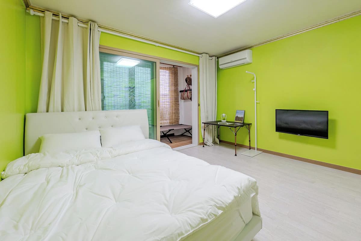Una habitación de hotel con cama, televisión, aire acondicionado y vistas a través de un ventanal.