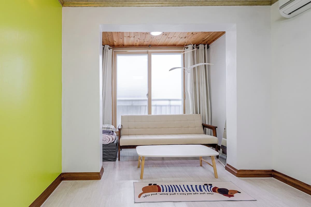 Una habitación con sofá, una mesita, una ventana con cortinas y vistas al exterior.
