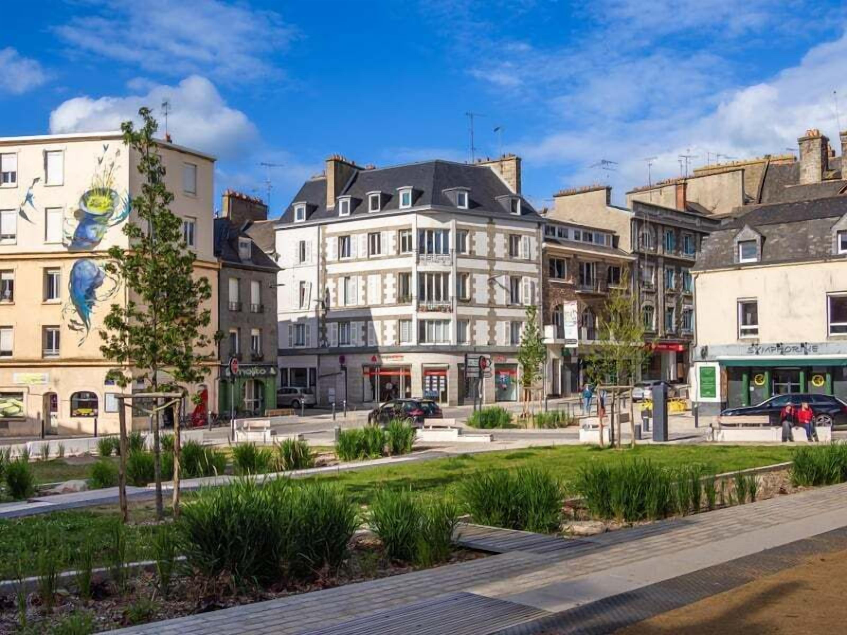 Une rue bordée d’immeubles, avec un trottoir et un espace verdoyant.