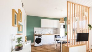 A compact kitchen with white cabinets, a washing machine, and a dining area with a table and chairs. - Near City Center & Train Station - Saint-Brieuc (Saint-Brieuc)