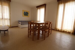 A dining area with a round table and six chairs, a sofa, a small cabinet, and a painting on the wall. - Coastal Comfort Retreat With Stunning Views (Lignano Sabbiadoro)