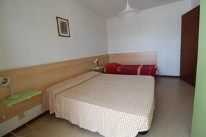 A bedroom with a bed, a bedside table, a lamp, a wall-mounted picture, and a door. - Coastal Comfort Retreat With Stunning Views (Lignano Sabbiadoro)