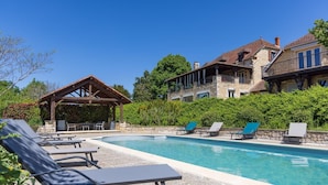A swimming pool with lounge chairs, a wooden pergola, and stone buildings with balconies. - Holiday home in Rouffilhac with private pool (ROUFFILHAC)