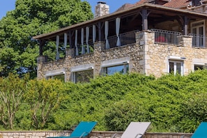 A stone building with balconies, a stone facade, and a lush green backdrop.