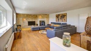 A modern living room with a stone wall, a fireplace, a sectional sofa, and a large window. - Holiday home in Rouffilhac with private pool (ROUFFILHAC)