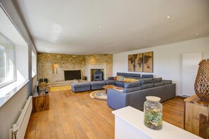 A modern living room with a stone wall, a fireplace, a sectional sofa, and a large window.