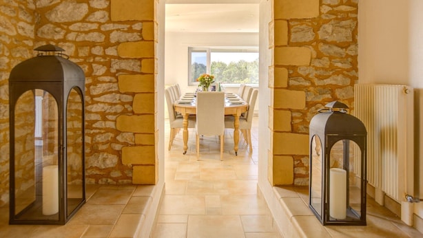 A stone-walled dining area with a table and chairs, two lanterns, and a view through a doorway. - Holiday home in Rouffilhac with private pool (ROUFFILHAC)