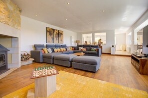 A living room with a sectional sofa, a fireplace, a chessboard, and a large window.