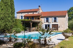 Ein Steinhaus mit Swimmingpool, einer Holzterrasse und einer überdachten Terrasse.