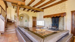 A living room with a stone fireplace, a sofa, a wooden staircase, and a television. - Holiday Home in Gramat near Padirac Cave (GRAMAT)