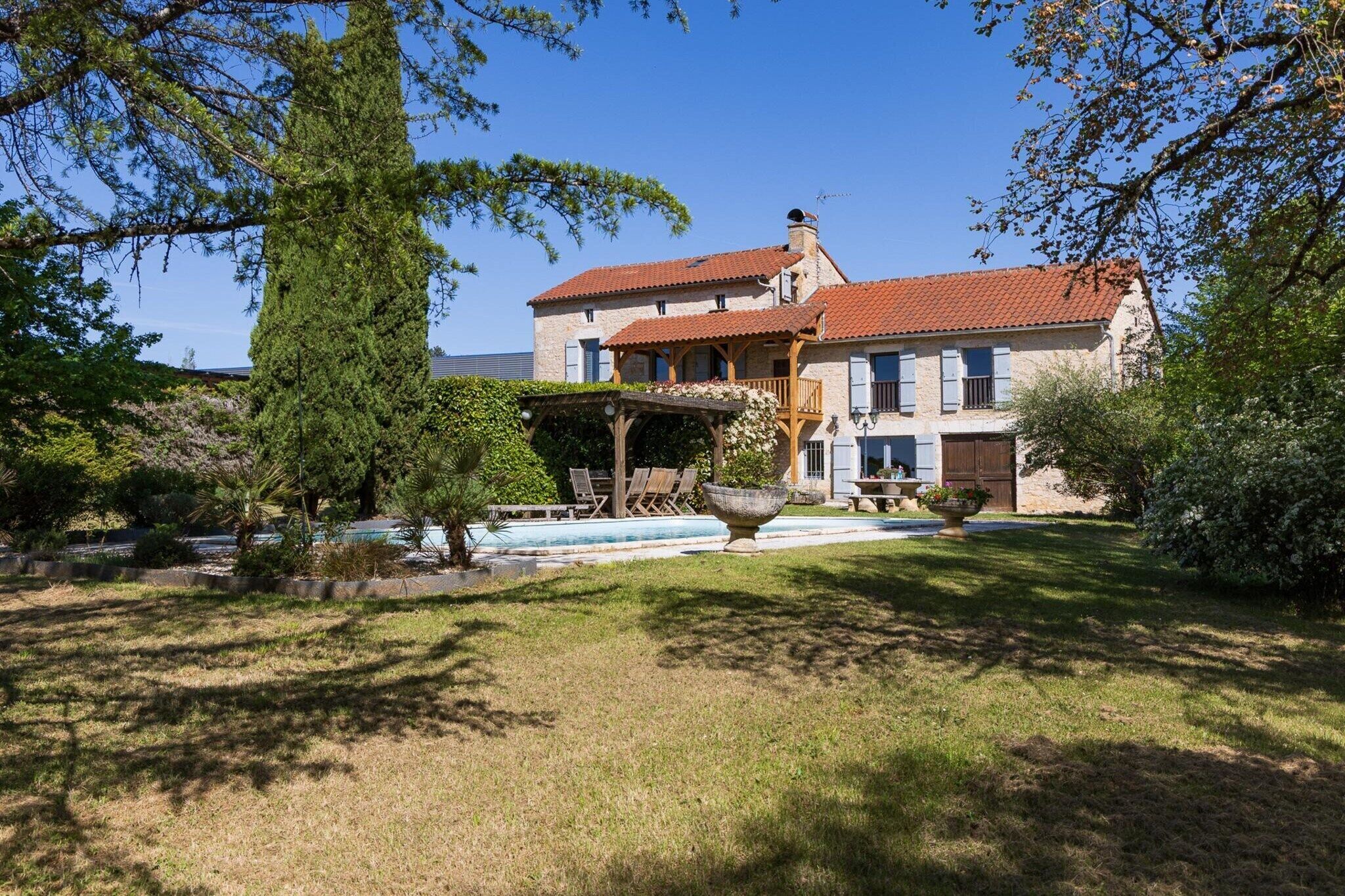 A two-story stone building with a red-tiled roof, a covered porch, and a swimming pool in the foreground.