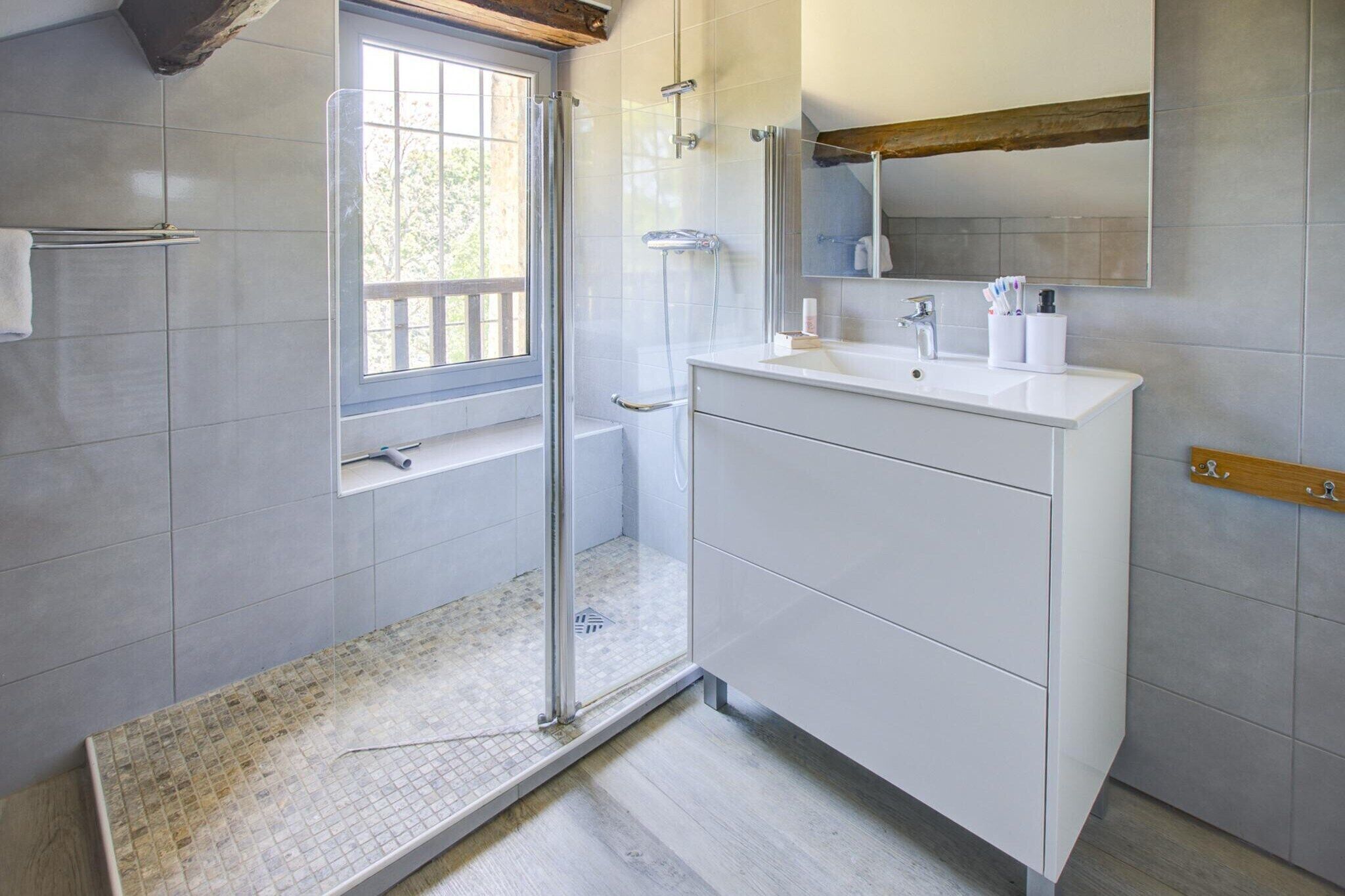 Een badkamer met een douche, wastafel, spiegel en raam.