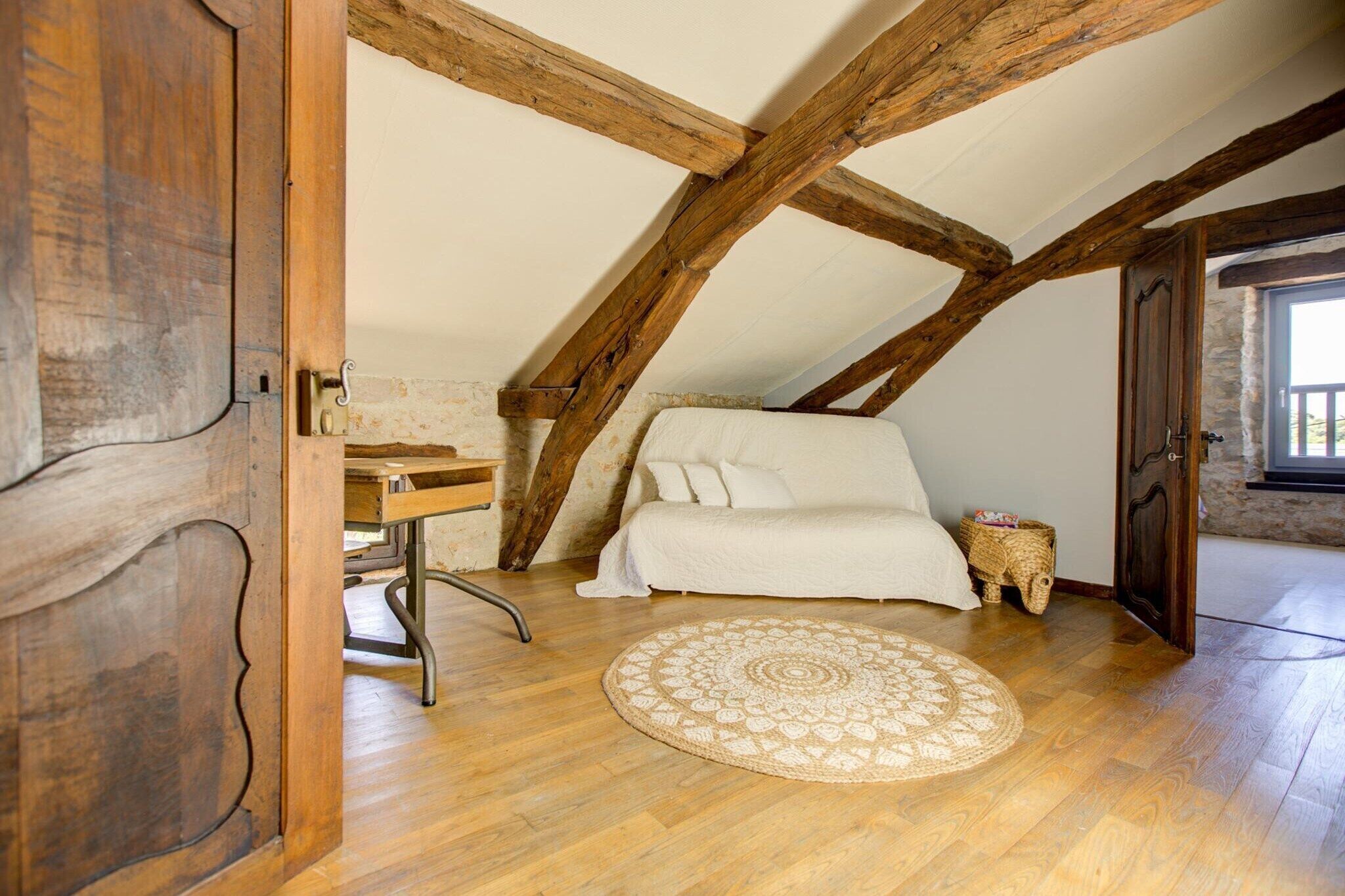 Une chambre à coucher aménagée dans un espace de type « loft », avec des poutres en bois apparentes, un lit, un bureau et un tapis rond.