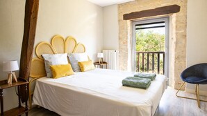 A bedroom with a large bed, a wooden headboard, a nightstand with a lamp, a chair, and a view of greenery outside. - Holiday Home in Gramat near Padirac Cave (GRAMAT)