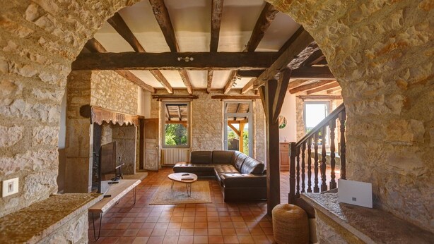A stone-walled room with a wooden ceiling, a sofa, a television, and a fireplace. - Holiday Home in Gramat near Padirac Cave (GRAMAT)