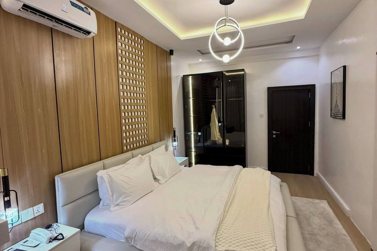 Une chambre moderne avec un grand lit, une armoire intégrée, un luminaire au plafond et un climatiseur fixé au mur.