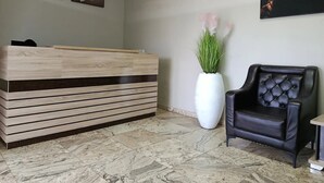 A reception desk, a black leather chair, a large vase with green plants, and three framed artworks on the wall. - THE EVOLUTION HOTEL (Gombe)