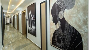 A hallway with framed artwork, doors, and a marble floor. - THE EVOLUTION HOTEL (Gombe)