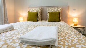 Un lit bien fait, recouvert d’une couvre-lit à motifs, avec deux oreillers et une serviette pliée. Deux lampes de chevet sont placées de chaque côté du lit.
