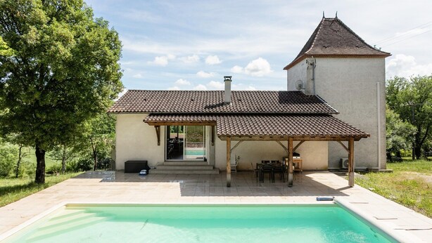 Une maison avec une piscine, un patio couvert et une petite structure en forme de tour.
