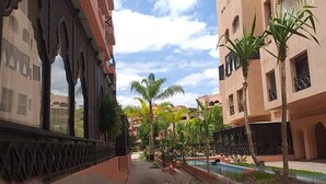 Ein Innenhof mit Pool, Palmen und Gebäuden mit Bogenfenstern und Balkonen.