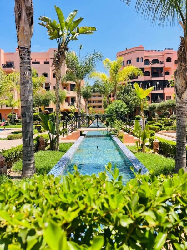 A pool surrounded by lush greenery and multi-story buildings with balconies. - Nice property Marrakech village with pools and Gardens (Marrakesh)