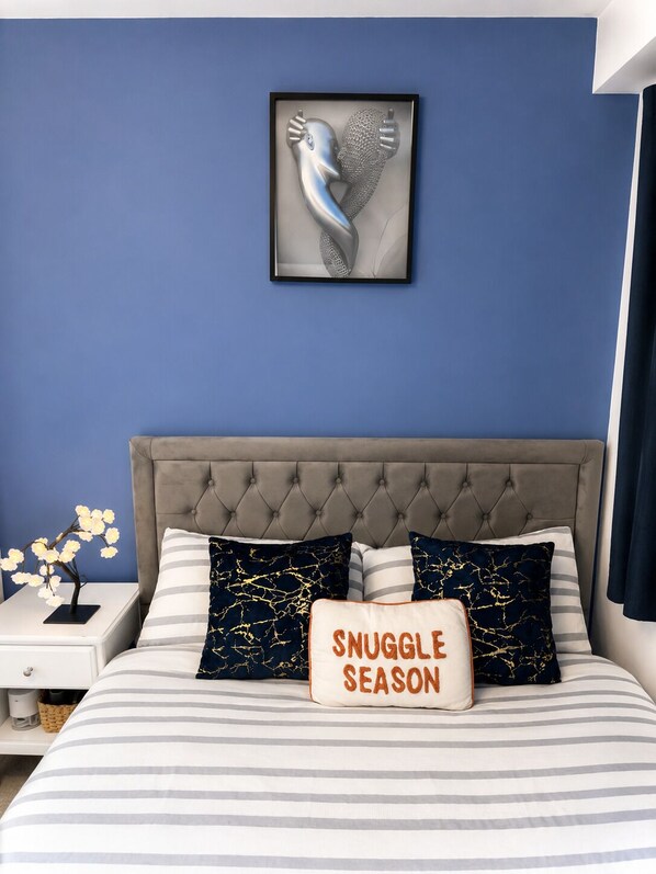 A bedroom with a tufted headboard, a framed artwork on the wall, and a pillow with 'SNUGGLE SEASON' text.