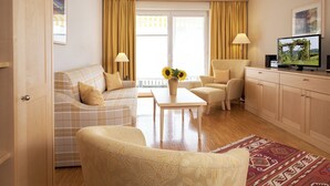 Een woonkamer met een bank, fauteuil, salontafel, televisie en uitzicht door het raam.