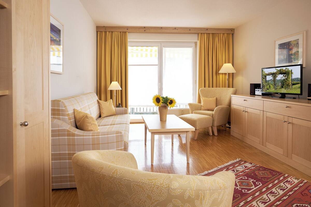 Una sala de estar con sofá, sillón, mesa de centro, televisor y vistas al exterior.