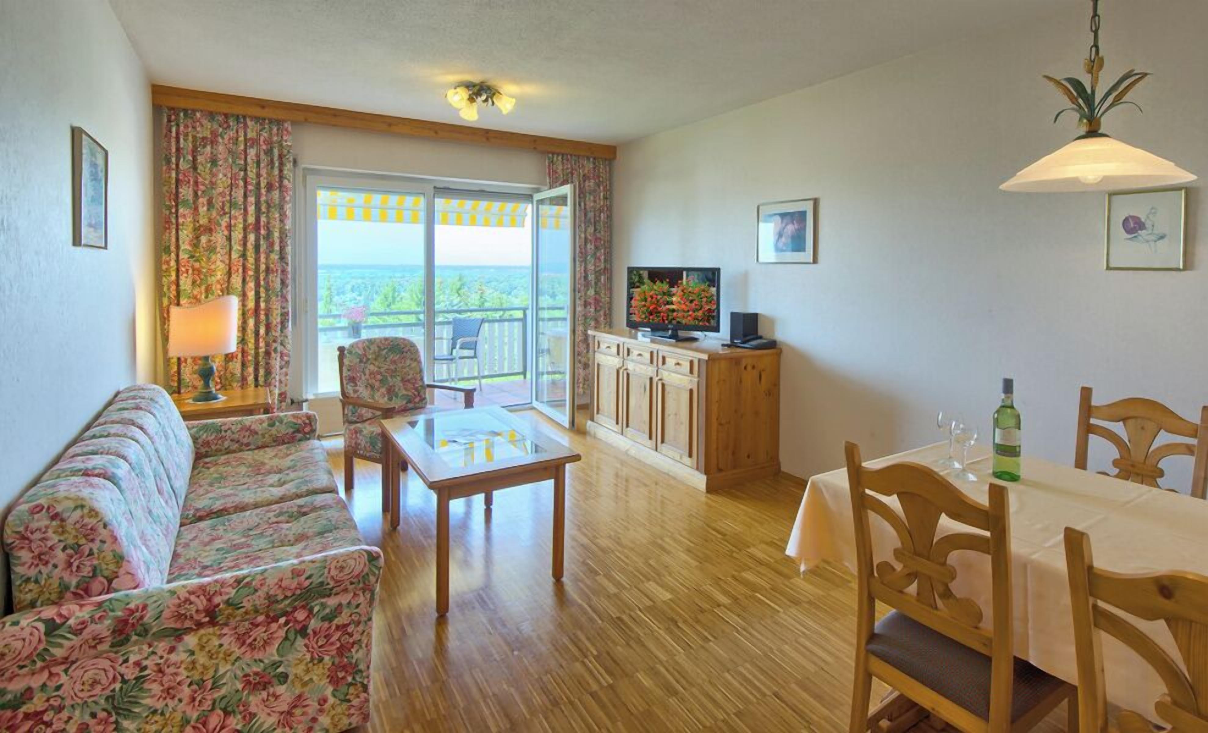 A living room with a sofa, a table, a television, and a balcony with a view.