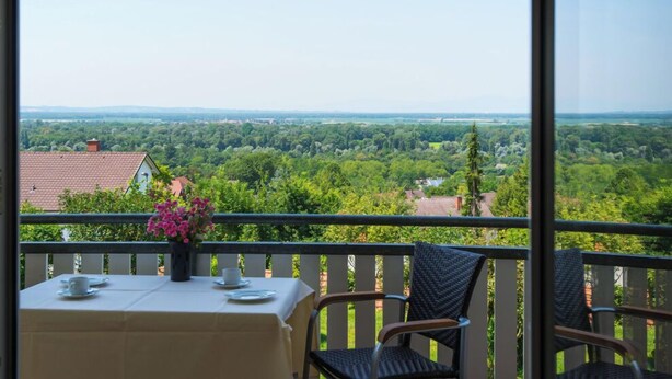 Een balkon met een eettafel, stoelen en uitzicht op een groen landschap.