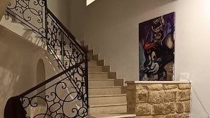 A staircase with ornate metal railings, a stone wall, a painting, a sofa, and a white table.