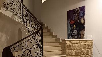 Un escalier avec des rampes en métal ouvragé, un mur en pierre, un tableau, un canapé et une table blanche.