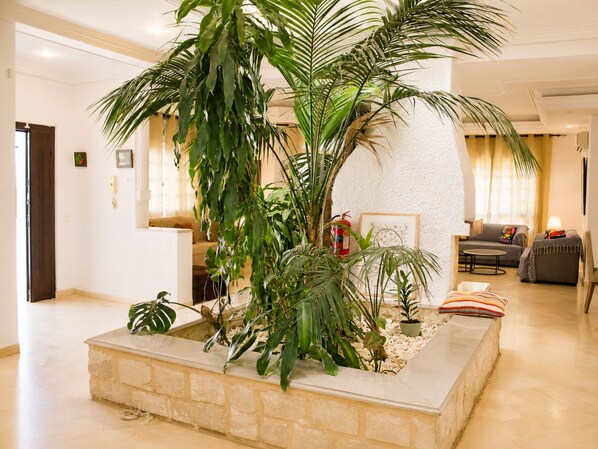 A lobby with a large indoor plant arrangement, a reception desk, and a seating area with sofas.