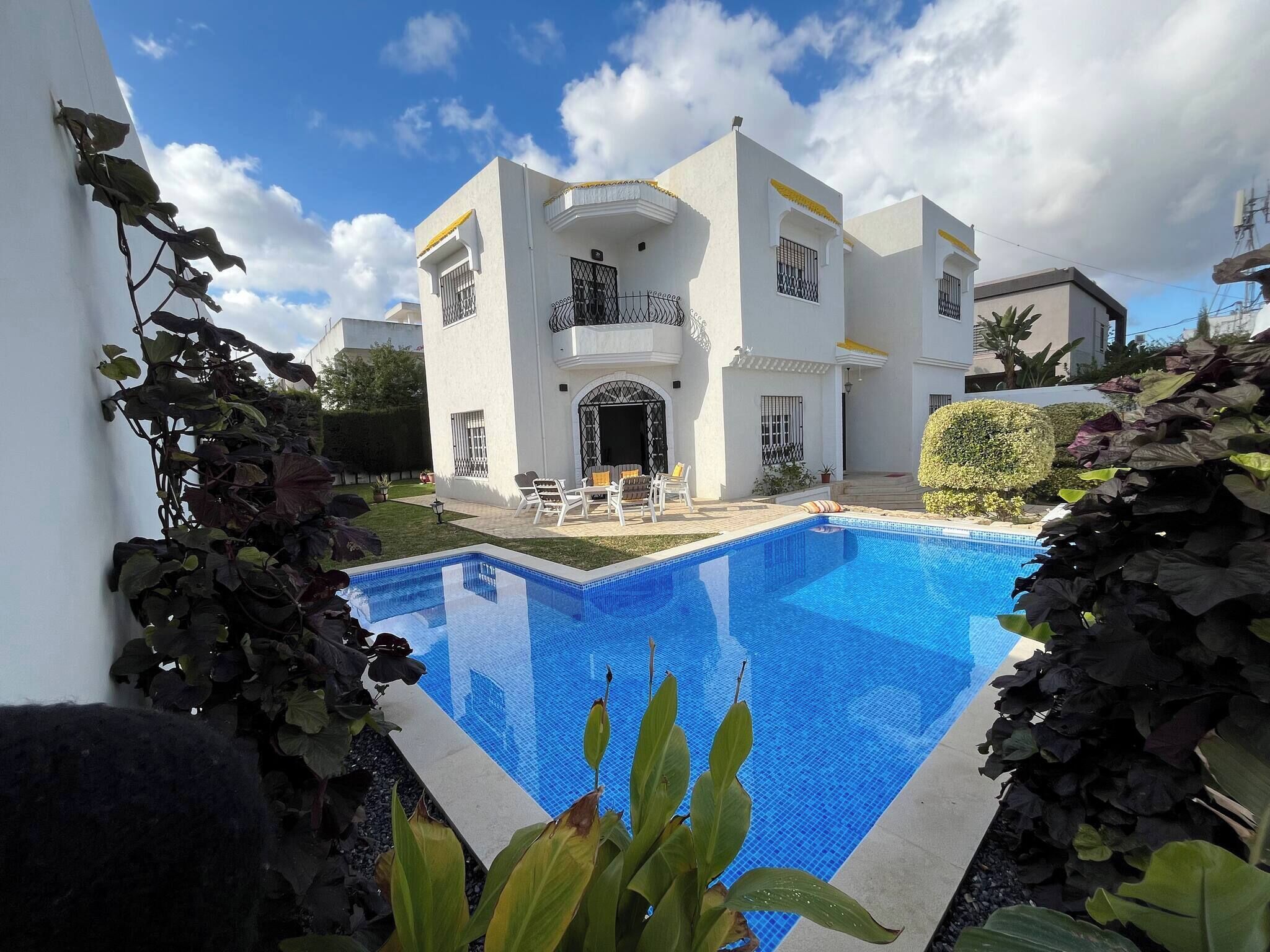 Un bâtiment moderne de couleur blanche, doté d’une piscine, d’un espace extérieur aménagé et d’un jardin bien entretenu.