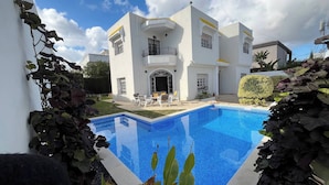 A modern white building with a swimming pool, outdoor seating, and a well-maintained garden.