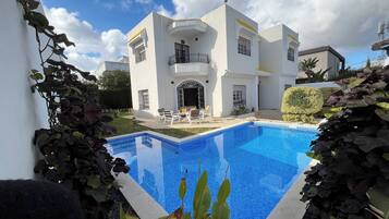 Un bâtiment moderne de couleur blanche, doté d’une piscine, d’un espace extérieur aménagé et d’un jardin bien entretenu.