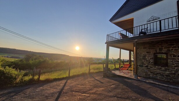A stone building with a balcony, a clear sky, and a sun setting in the background. - Les herbes folles de Oizy, bed and breakfast with terrace in the Ardennes. (Oizy)