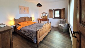 A bedroom with a wooden bed, bedside lamps, a dresser, a chair, a window with shutters, and a mirror on the wall. - Les herbes folles de Oizy, bed and breakfast with terrace in the Ardennes. (Oizy)
