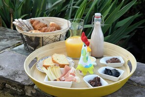 A breakfast setup with bread, pastries, cheese, ham, and a drink on a wooden table.