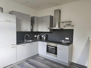 Una cocina moderna con armarios blancos, una campana extractora de acero inoxidable, horno empotrado y encimera negra.