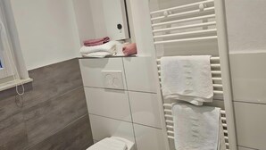 Moderni kylpyhuone, jossa on valkoinen allaskaappi, pyyhekoukku ja peili.
