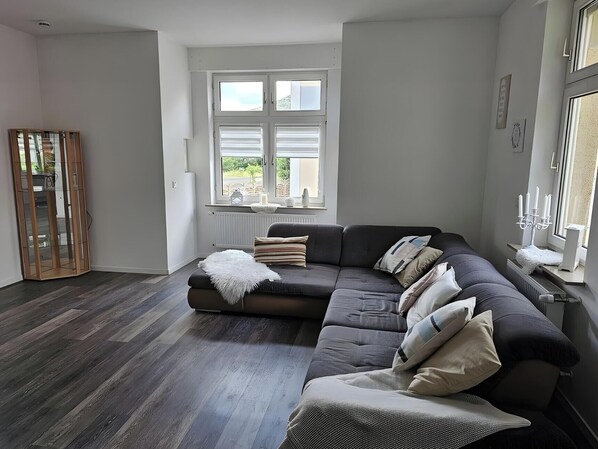 A modern living room with a sectional sofa, a glass cabinet, and a large window with blinds. - Holiday Home 'Ritah' with Shared Terrace, Private Garden and Wi-Fi (Idar-Oberstein)