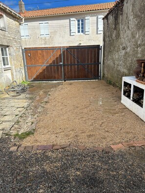Ein Schotterweg führt zu einer Holztür einer Garage, mit einer Betonkonstruktion auf der rechten Seite und einer Steinmauer links.