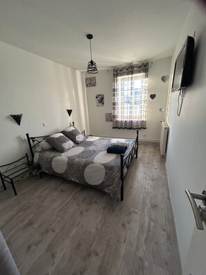 Ein Schlafzimmer mit Bett, Fernseher und einem Fenster mit Vorhängen.